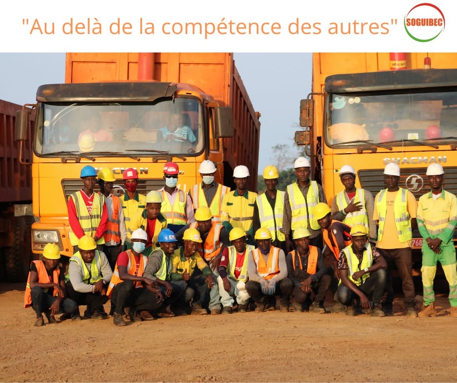 Les équipes de la SOGUIBEC, en casques et gilets de sécurité, posant devant ses camions-bennes Shacman